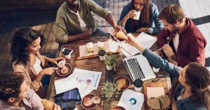 A group of people sitting around a table at a coffee shop, enjoying a variation of hot drinks and pastries.