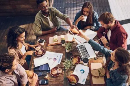 A group of people sitting around a table at a coffee shop, enjoying a variation of hot drinks and pastries.