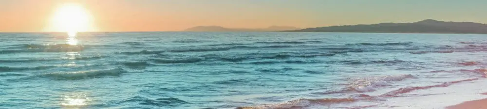Clear beach sand and water with sun setting in background.