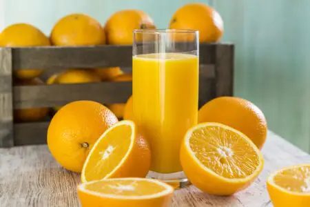 Glass of orange juice with oranges next to the glass.