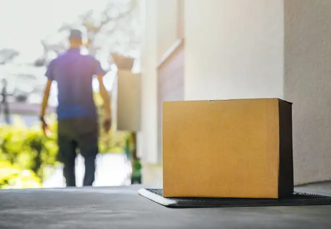 Parcel on doorstep with a delivery driver walking away.