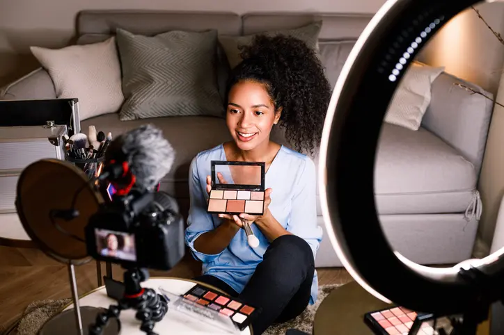 A beauty influencer shows off a colour cosmetic pallet in front of a camera.