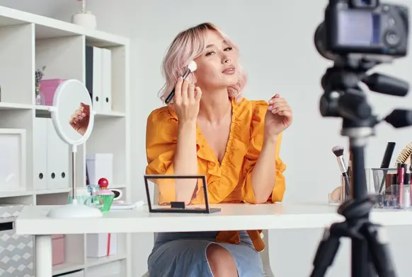 A beauty influencer applies make up in front of a camera.