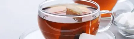 Clear tea glass is filled with black tea and has a black tea bag floating in it.