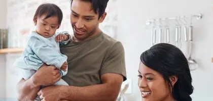 An Asian family consisting of a mum, dad and baby are standing together in the kitchen.
