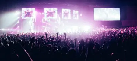 Concert crowd with their arms up and purple spotlights illuminating the scene.
