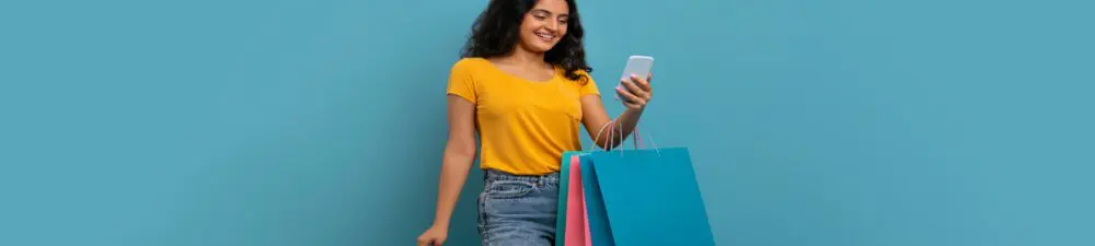 Gen Shopper, carrying several shopping bags and scrolling on their phone.