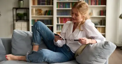 Woman relaxing on a sofa, holding her smartphone and credit card in her hands.