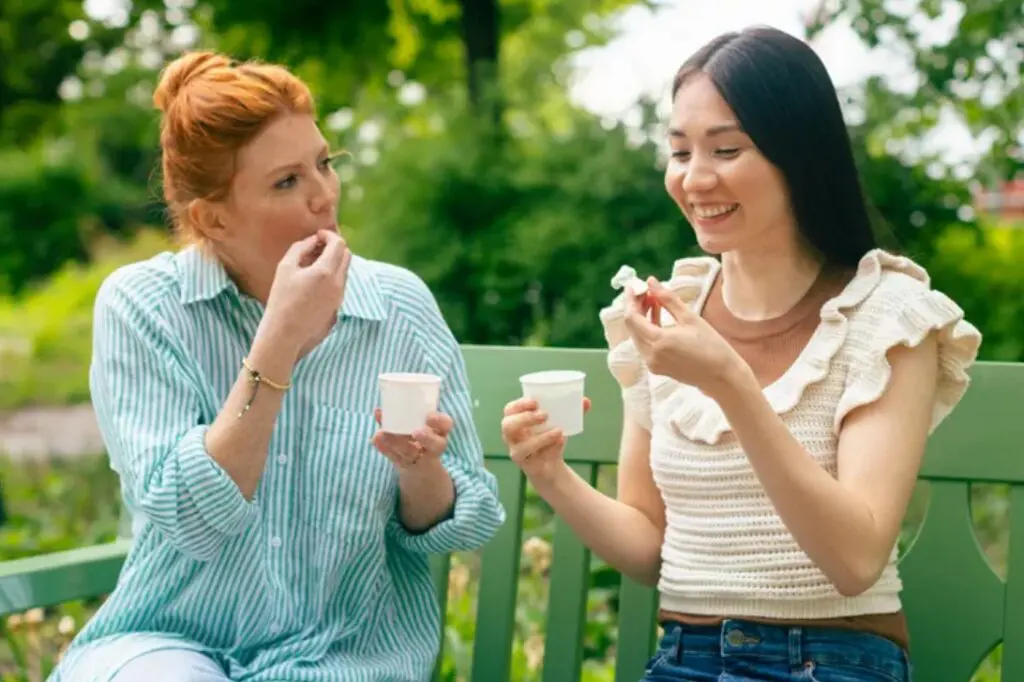 Two women sitting on a park bench, eating ice cream from Huhtamaki's molded fibre ice cream cups.