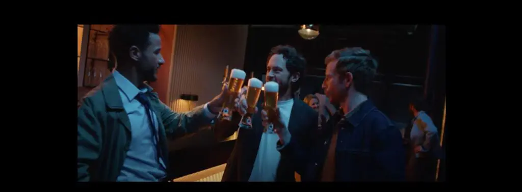 Screenshot des Warsteiner Werbespots: Drei Männer stoßen in einer Bar mit Biergläsern an.
