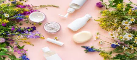 Beauty-Produkte in minimalistischer Verpackung auf rosamen Untergrund und Blumen/Pflanzen an beiden Rändern.