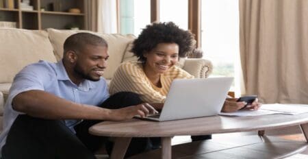 young Black couple using laptop, looking at screen, smiling