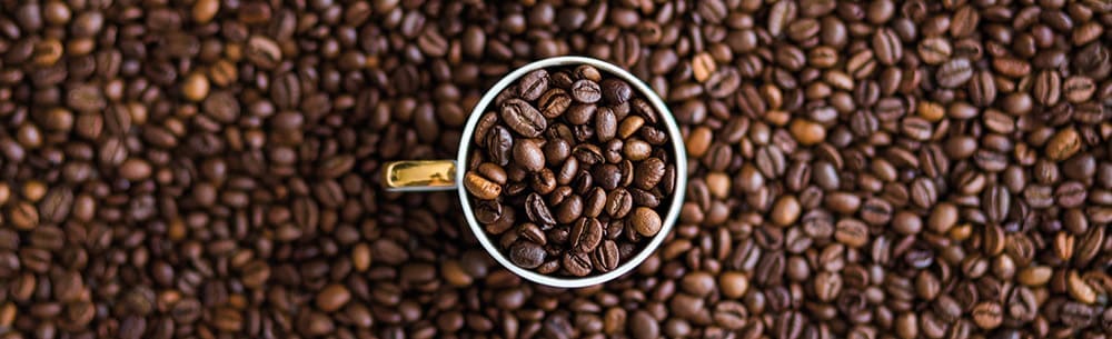 A cup filled with coffee beans in a sea of coffee beans. Photo taken from above.