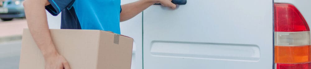 Man holding a parcel with one hand on his white van door