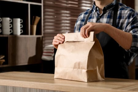 man behind counter holding a paper takeaway bag