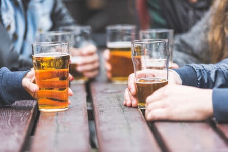 A picnic table with several pints of beer sat on it, with hands around the table holding the drinks.