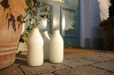 Three glass milk bottles outside a house with a blue door.