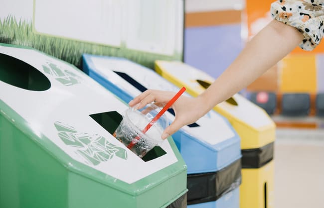 Three recycling bins with someone throwing away a plastic drink