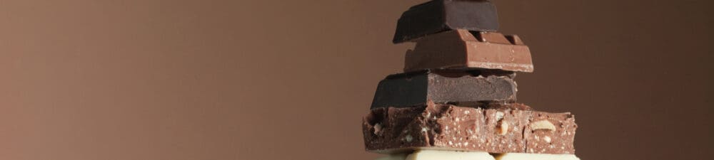 Stack of milk, dark and white chocolate on a brown background