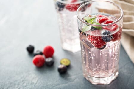 A glass of sparkling water with blueberries, raspberries, and a sprig of mint.