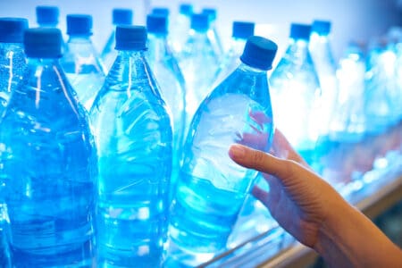 A hand pulling a bottle of water out of a refrigerator stocked full of bottled water.