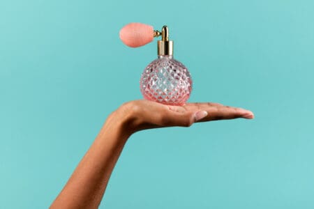 Pink perfume bottom on a hand with light blue background