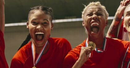 Four sportswomen celebrate their win on a football pitch.
