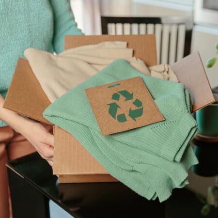 A cardboard box with some folded clothing items inside and a sign with a recycling sign printed on it.