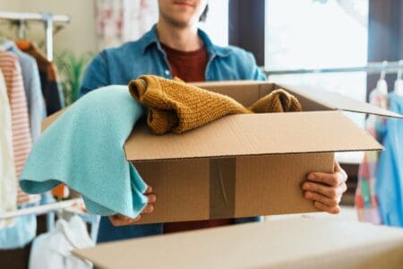 Individual carrying a cardboard box with some items of clothing hanging over the brim of the box.