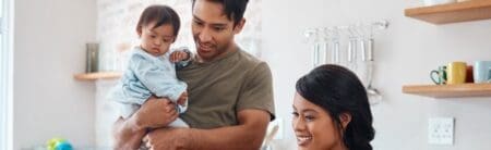 An Asian family consisting of a mum, dad and baby are standing together in the kitchen.
