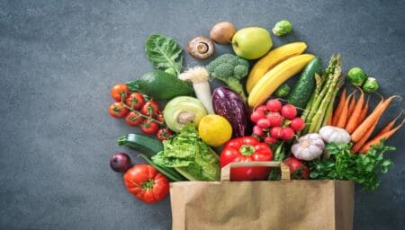 Groceries spilling out of a paper bag on grey background.