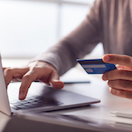 A person (out of frame), typing on a laptop and holding a credit card.
