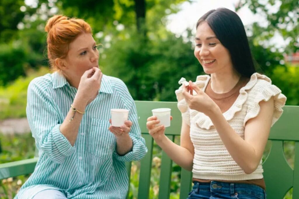 Two women sitting on a park bench, eating ice cream from Huhtamaki's molded fibre ice cream cups.