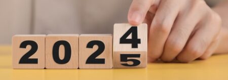Holzböcke mit Zahlen darauf, die „2024“ buchstabieren. Der letzte Block „4“ wird von einer Person auf „5“ umgedreht.